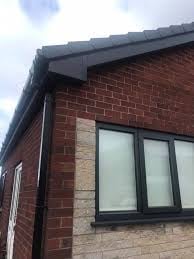 Modern brick building corner with black-framed window and dark roofline against cloudy sky