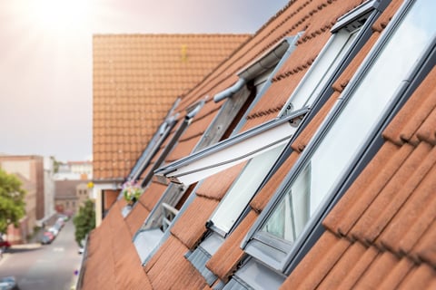 Open roof windows on a brick residential building with terracotta tiles and an urban street view in the background