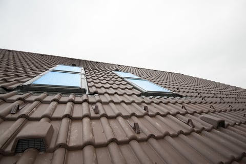 Two rectangular skylights installed in a brown ceramic tile roof photographed from below against a cloudy sky