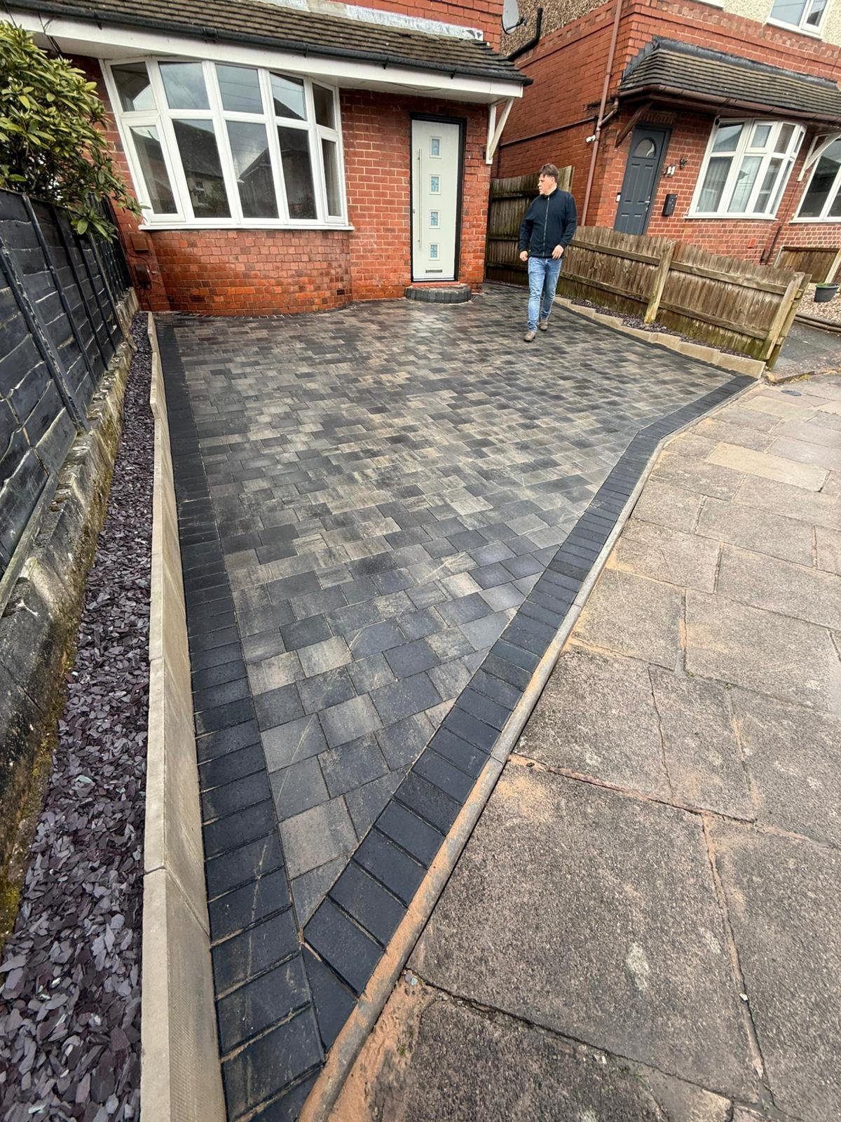 Newly paved driveway with geometric pattern in front of brick house with white trim and bay window